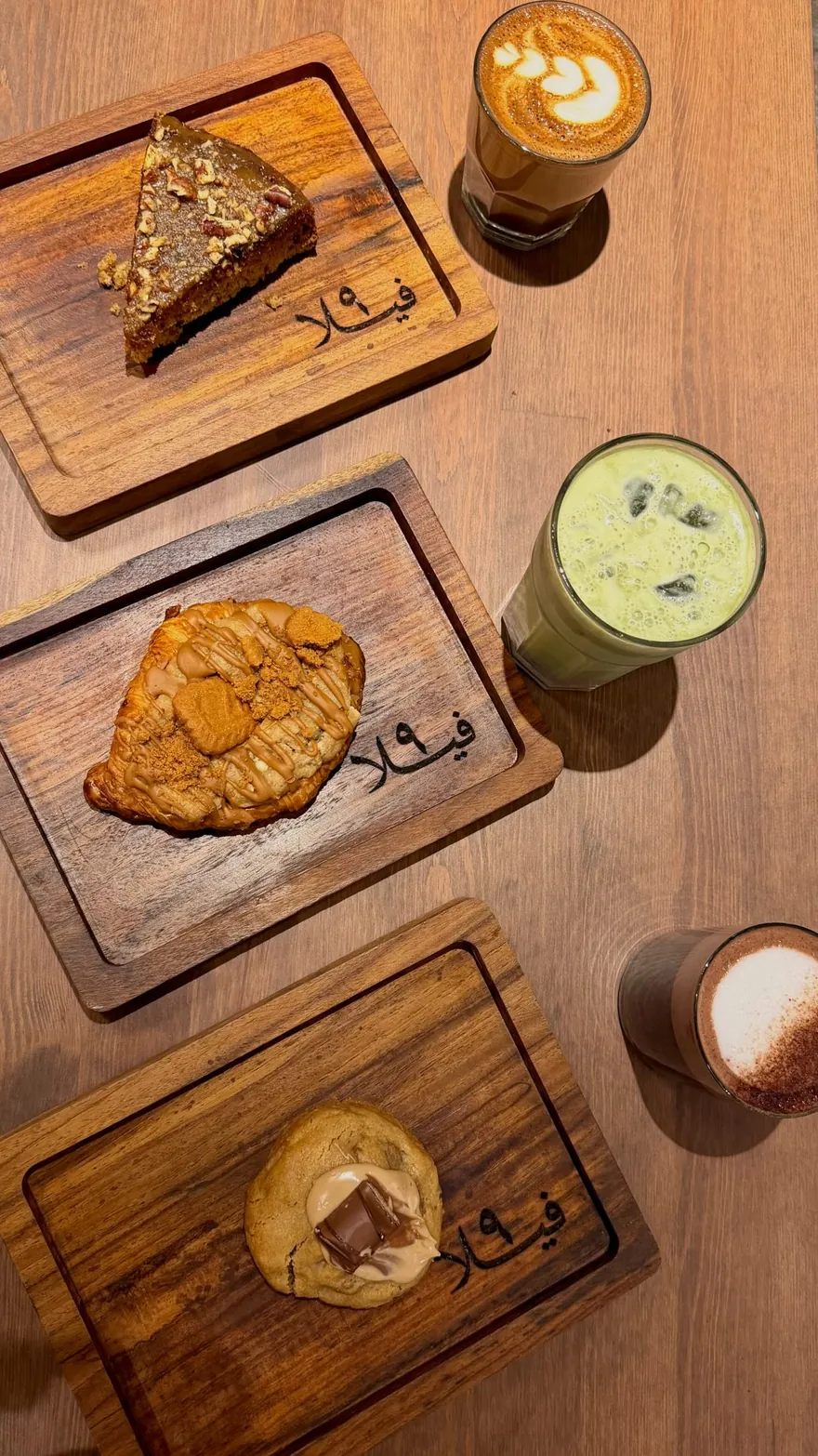 A flat-lay of Villa 9 boards: carrot cake, a cookie, a croissant, an iced matcha, a latte and a cortado.