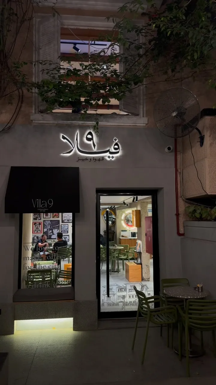 Villa 9 at night: the backlit فيلا ٩ sign above a lit doorway, with olive-green chairs on the terrace.